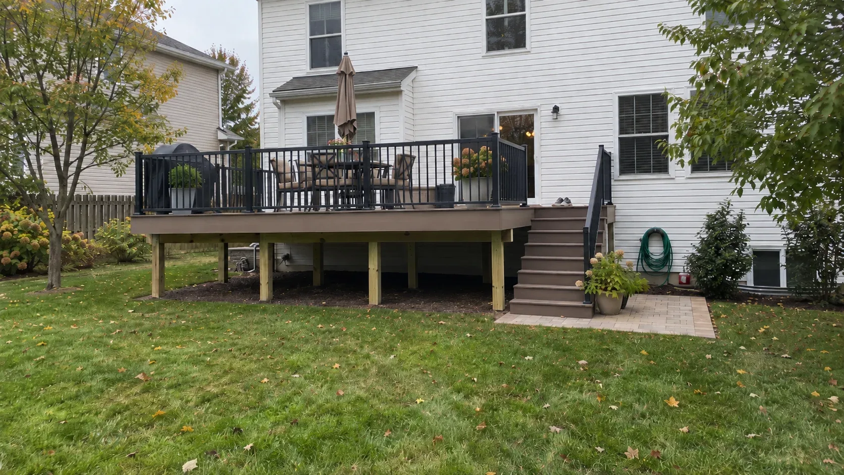 A composite deck lifted above the grass, framed by dark railings, seen from the garden
